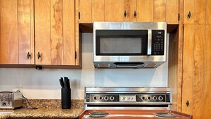 A kitchen with wooden cabinets, a stainless steel dishwasher, an orange stove, and a microwave.