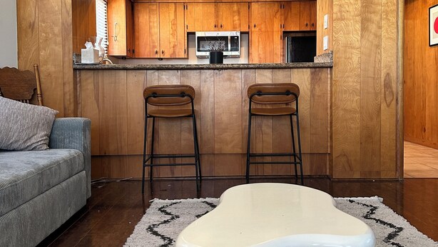 A modern kitchen with wooden cabinetry, a microwave, and two bar stools.