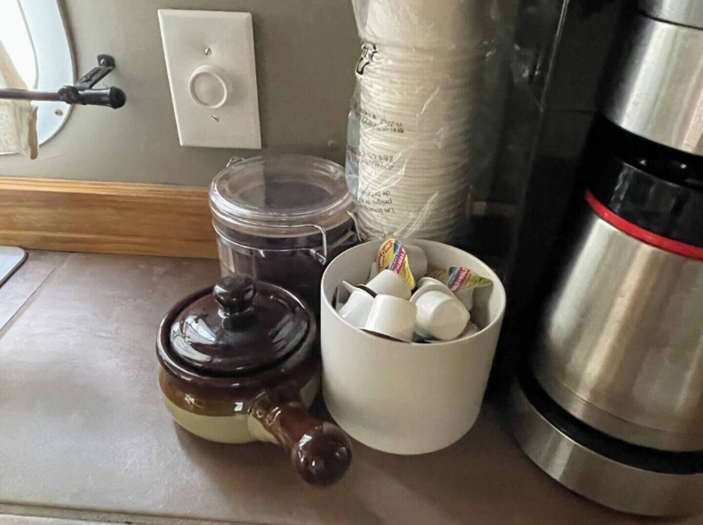 Un comptoir de cuisine avec une machine à café, une théière et un récipient contenant des sachets de thé.