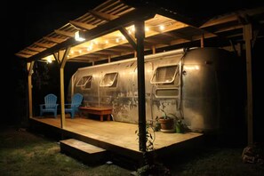 A covered outdoor area with a vintage trailer, blue chairs, and a wooden table. - Country setting in South ATX! (Austin)