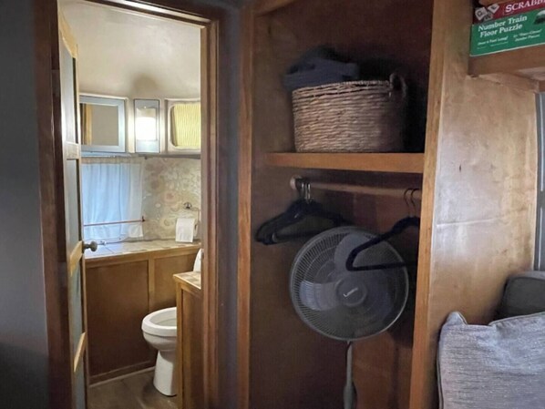A compact bathroom with a toilet, a small sink, and a fan on a wooden shelf. - Country setting in South ATX! (Austin)