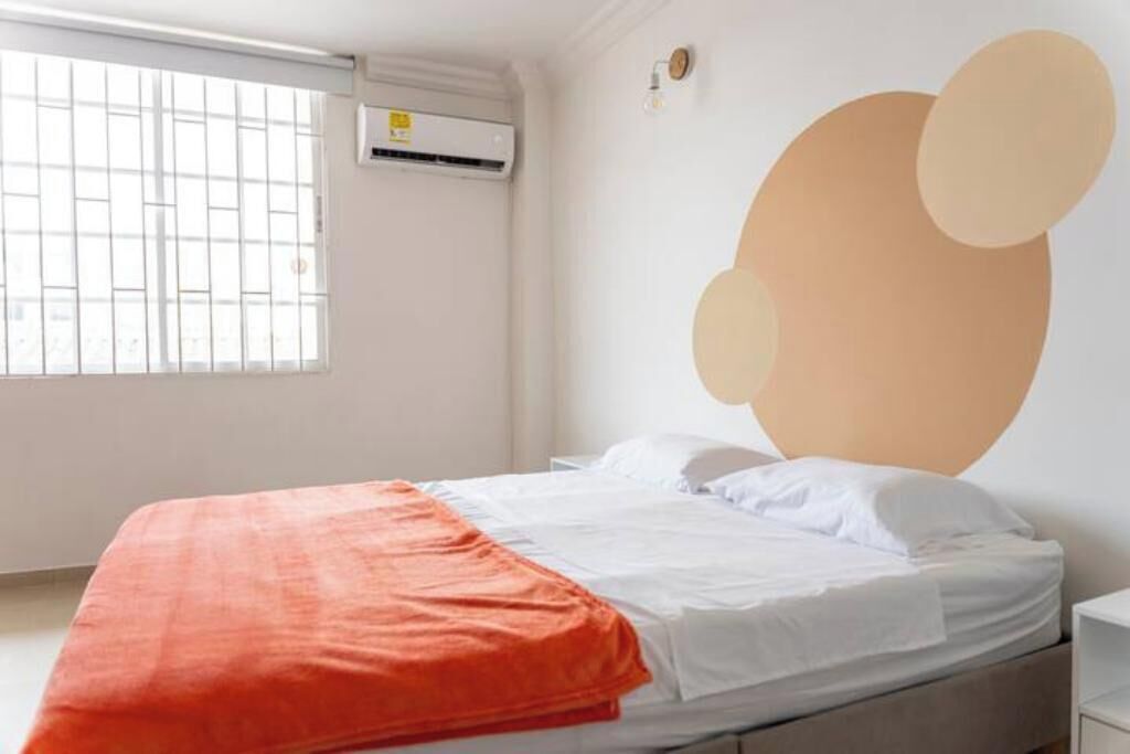 Une chambre à coucher avec un lit, un climatiseur, une fenêtre avec des barreaux et un mur orné de motifs abstraits.