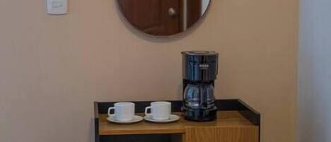 A small wooden cabinet with a mirror above it, containing two white cups and a coffee maker.