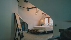 Een slaapkamer met een schuine kap, een bed met een witte dekbedovertrek, een accentmuur van steen en hangende hanglampen.