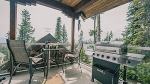 Een terras buiten met een barbecue, stoelen en een tafel.