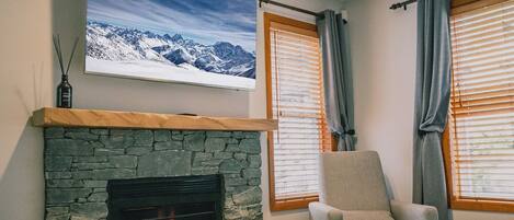 A bedroom with a stone fireplace, a mounted TV, and a bed.