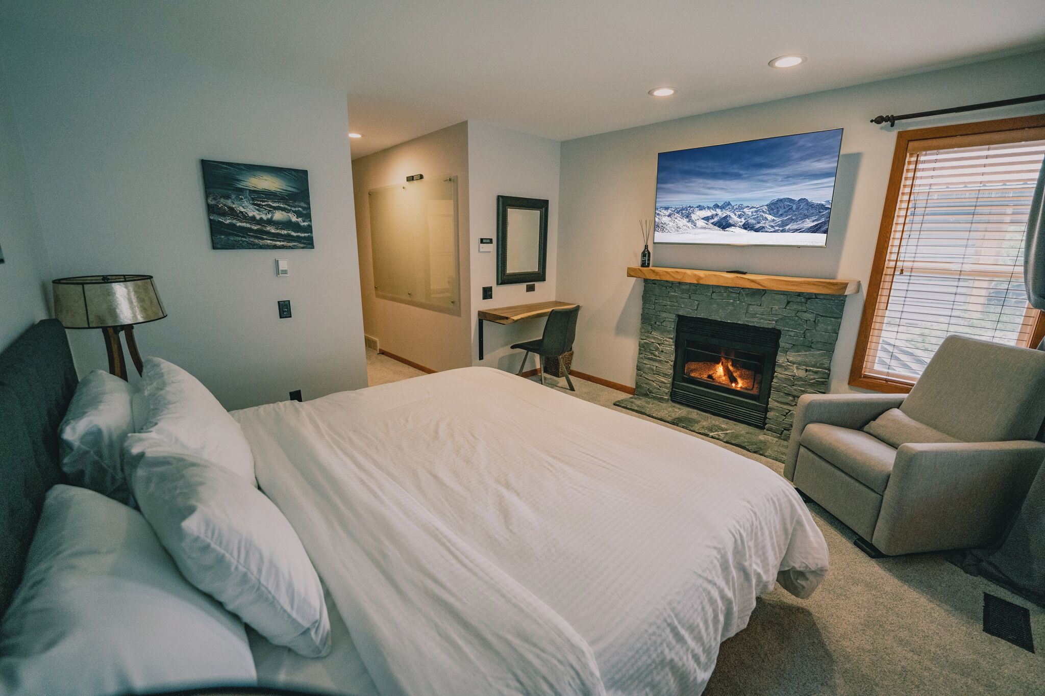 A bedroom with a large bed, a fireplace, a desk, and a chair.
