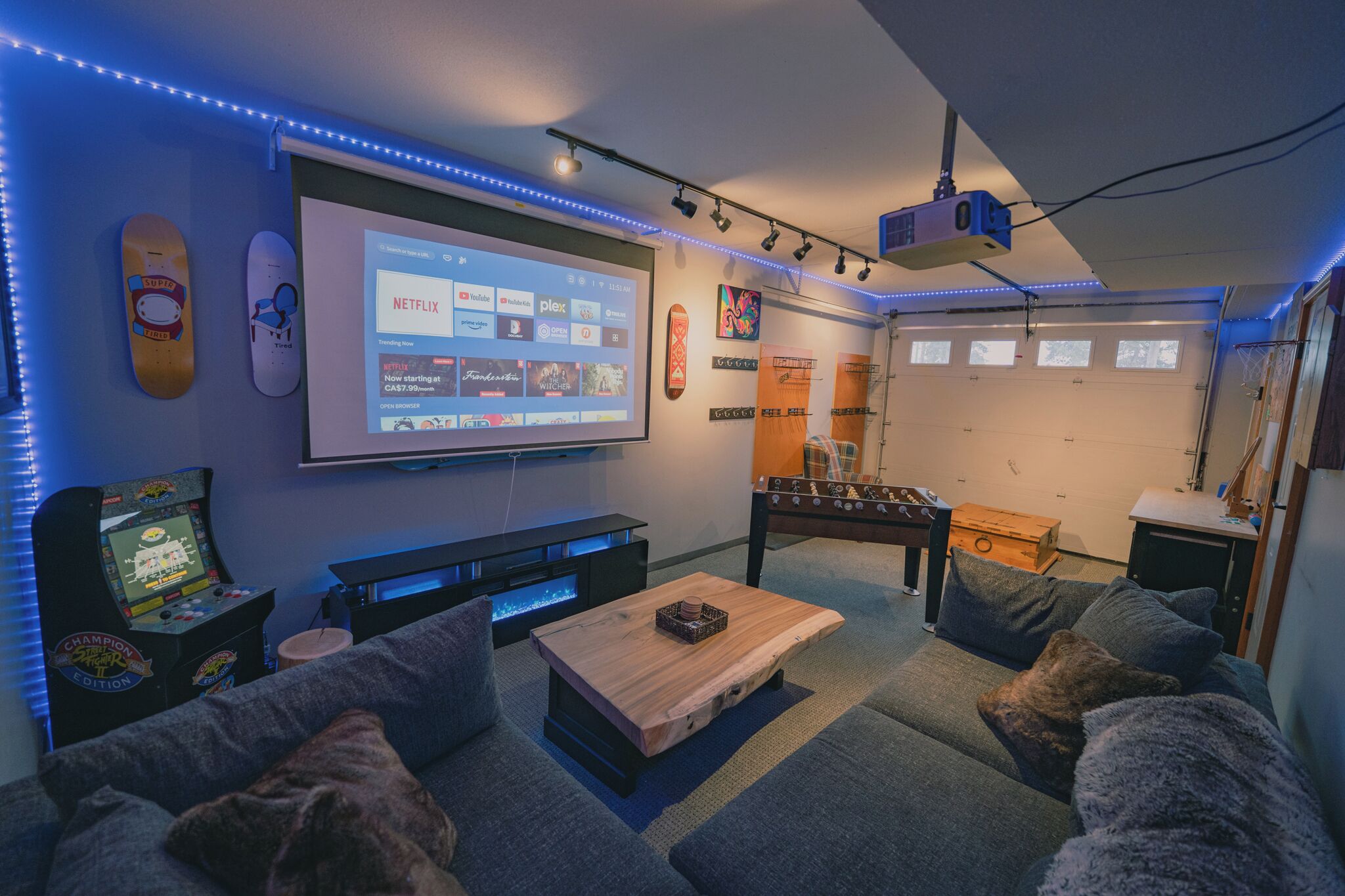 Ein gemütliches Wohnzimmer mit großem Fernseher, Spielkonsole und bequemen Sitzmöglichkeiten.