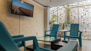 Une pièce avec un téléviseur fixé au mur, une table en verre et des chaises bleues.