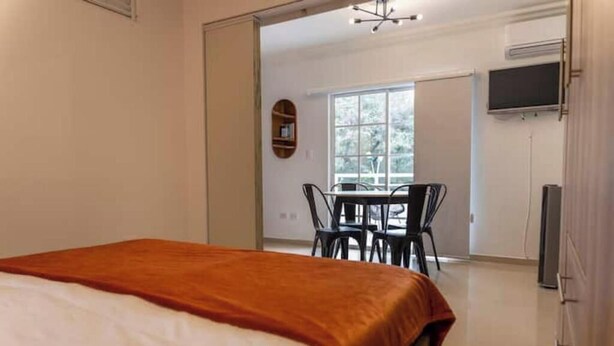 Une chambre d’hôtel comprenant un lit, un coin repas avec des chaises et une table, un téléviseur et une fenêtre donnant sur des arbres.