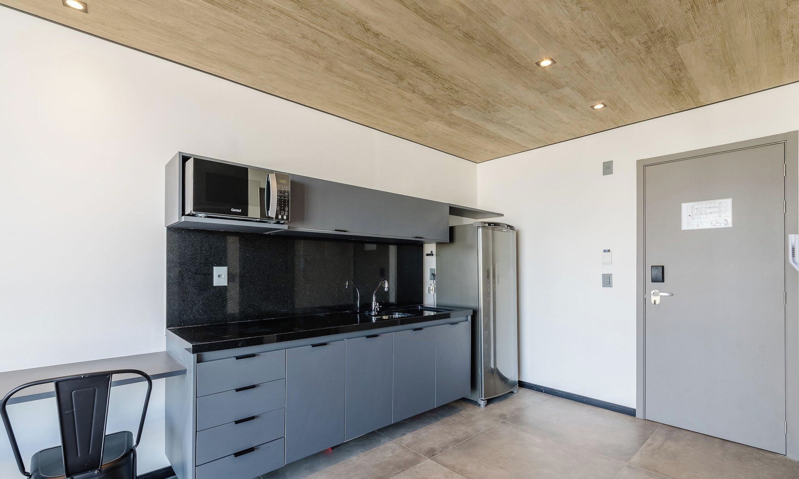 Una cocina moderna con encimera negra, armarios grises, refrigerador de acero inoxidable y un microondas.