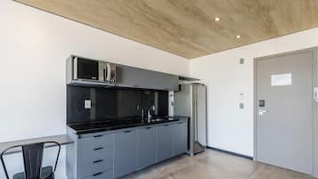 Una cocina moderna con encimera negra, armarios grises, refrigerador de acero inoxidable y un microondas.