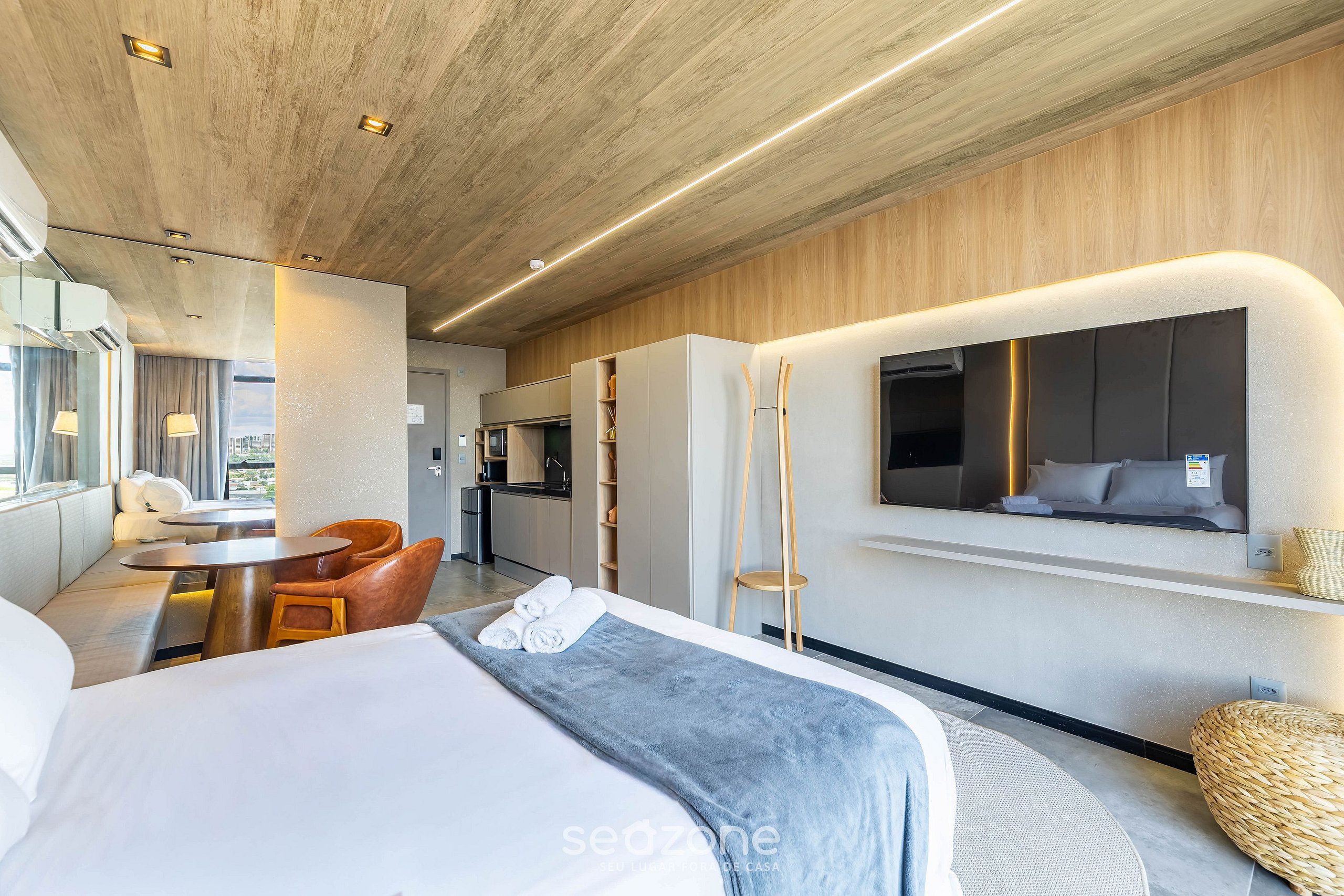 A modern hotel room with a large bed, a dining area, and a kitchenette.
