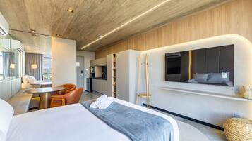A modern hotel room with a large bed, a dining area, and a kitchenette.