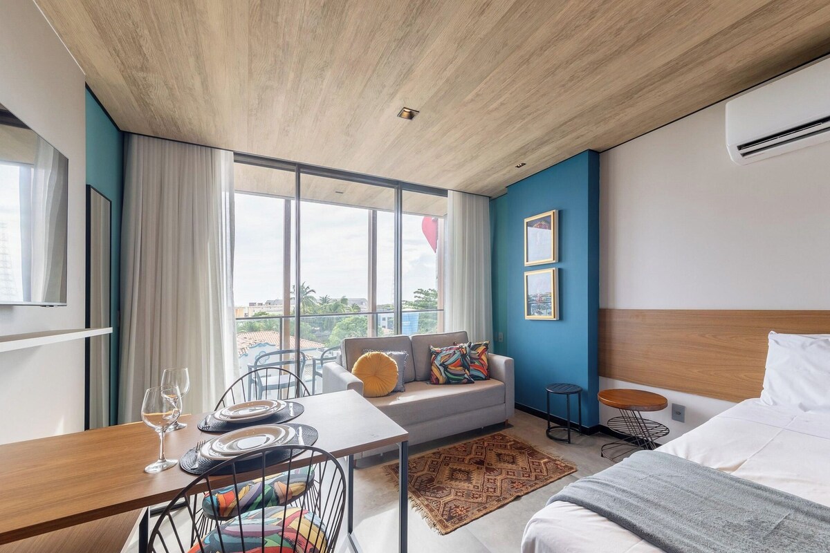 Una habitación de hotel moderna con un ventanal grande, un sofá, una mesa de comedor para dos personas y una cama.