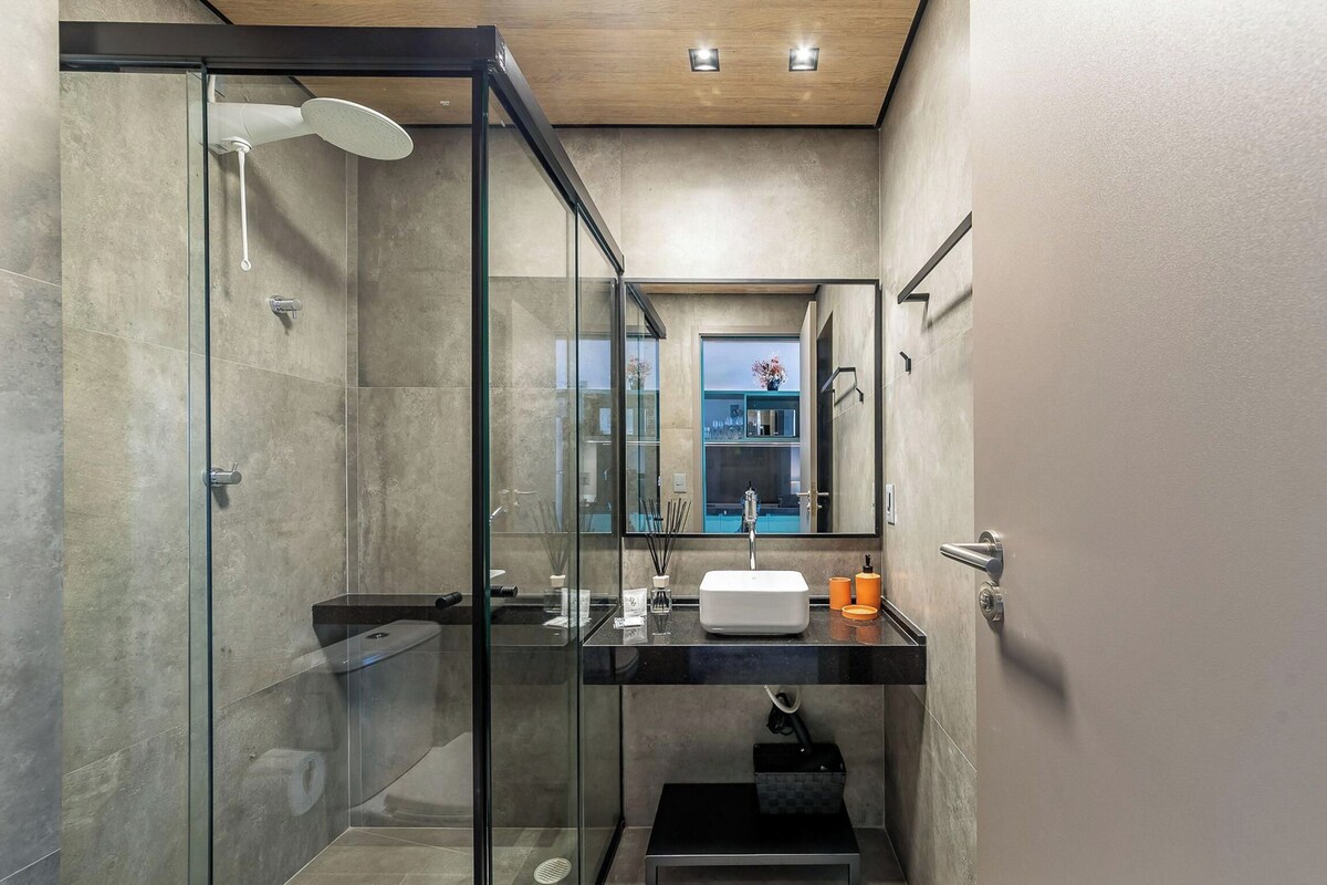 A modern bathroom with a glass shower enclosure, a black countertop sink, and a mirror above it.