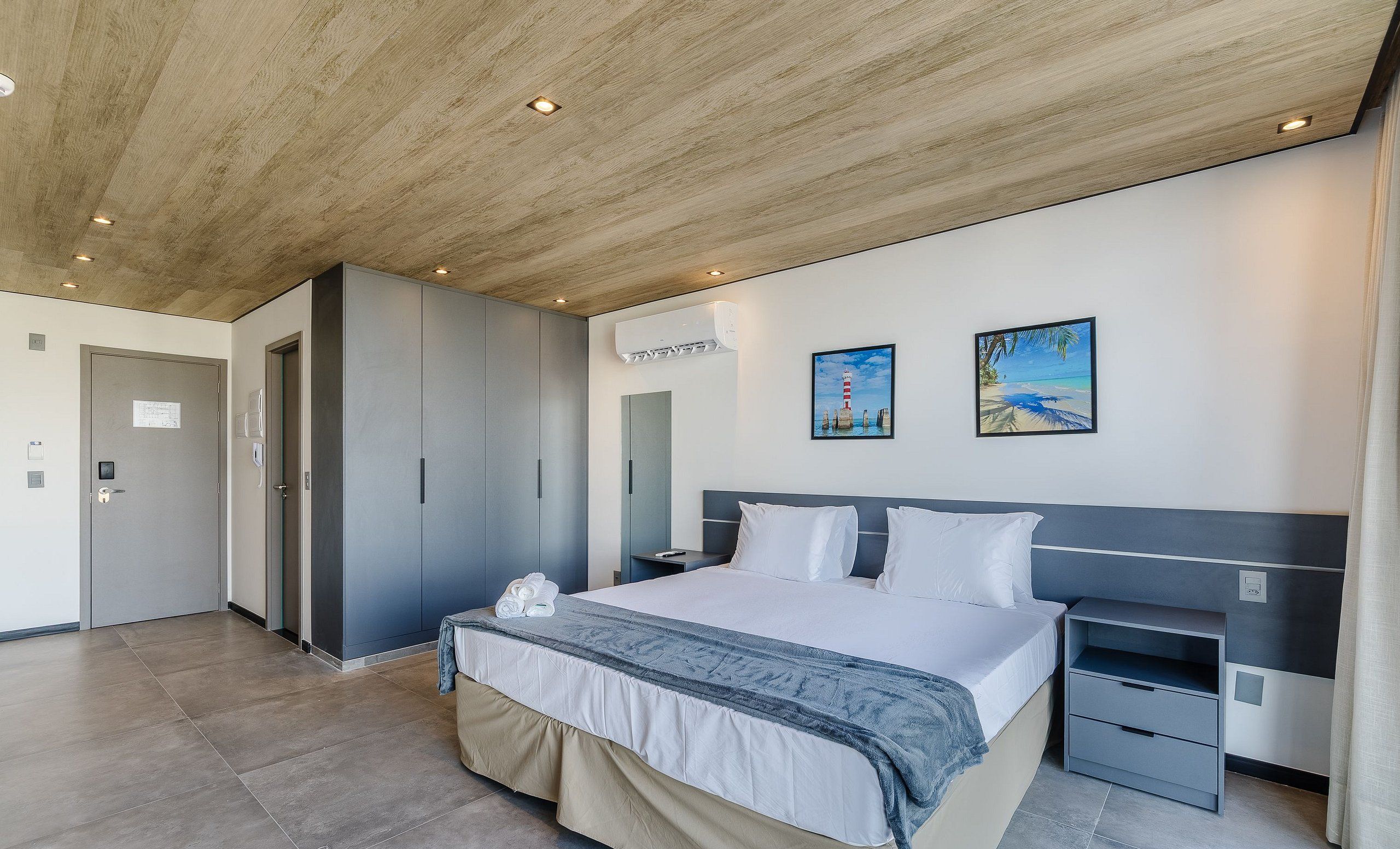 Una habitación de hotel moderna con cama, mesitas de noche, armario y un amplio ventanal con vista a la playa.