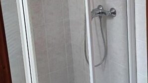 Un box de ducha con paredes de vidrio, un cabezal de ducha de mano y un grifo empotrado.