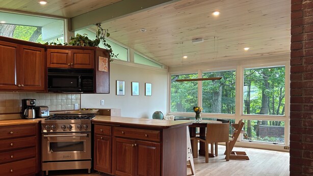 A modern kitchen with wooden cabinets, stainless steel appliances, and large windows offering a view of the outdoors. - Centrally Located Bright Family Home with Peaceful Natural Views and Central A/C (Burlington)