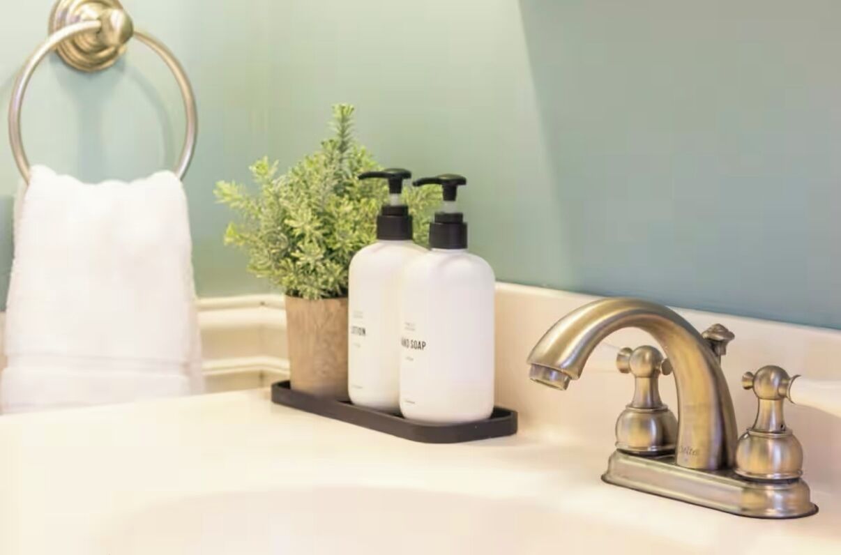 Un lavabo de salle de bain avec un robinet doré, une serviette blanche et deux flacons de savon blancs sur un plateau noir.