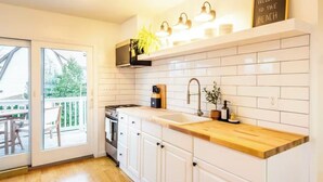 Une cuisine moderne avec des armoires blanches, un plan de travail en bois et un four encastré. Une grande fenêtre offre une vue sur l’extérieur.