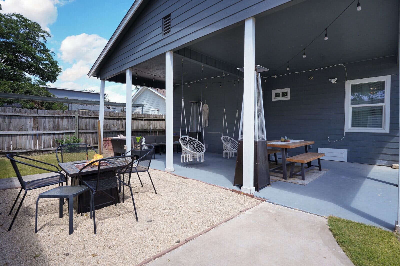 A covered patio area with outdoor furniture, including a table and chairs, and a hanging chair.