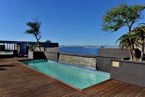A rooftop pool with clear blue water, surrounded by wooden decking and stone walls. - Stylish Green Point Apartment | Rooftop Pool (Cape Town)