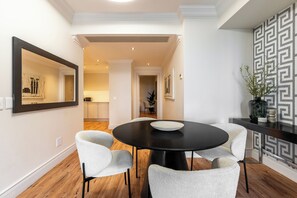 A dining area with a round black table and four white chairs, a black-framed mirror, and a geometric-patterned wall. - Stylish Green Point Apartment | Rooftop Pool (Cape Town)