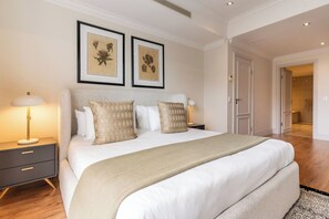 A neatly arranged bedroom with a large bed, two bedside tables with lamps, and framed botanical prints on the wall. - Stylish Green Point Apartment | Rooftop Pool (Cape Town)