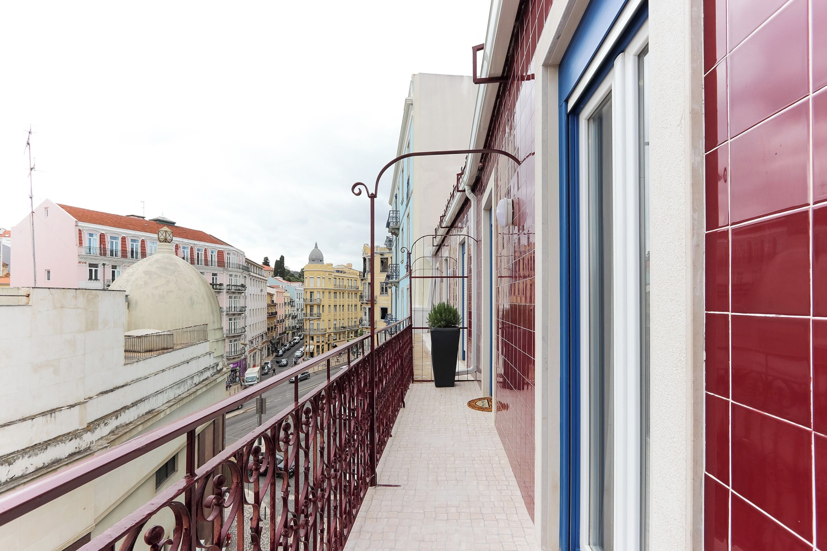 A narrow balcony with a metal railing overlooking a street with buildings and a river.