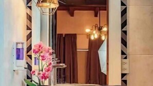 A modern bathroom with a geometric patterned wall, a wooden vanity, a large round sink, and pendant lighting.