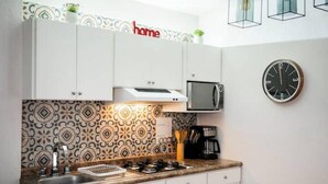 A kitchen with white cabinets, a patterned backsplash, a microwave, a stove, and a clock on the wall. - Modern, upscale loft one block from the walkway (San Cristobal d elas Casas, Chiapas)