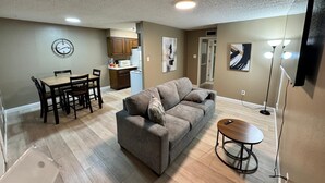 A living room with a gray sofa, a dining table with chairs, a kitchen area, and artwork on the walls. - 1BR Hideaway • Calm & Private (Beaumont)