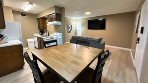 A compact kitchen with a dining table and chairs, a built-in oven, and a flat-screen TV mounted on the wall. - 1BR Hideaway • Calm & Private (Beaumont)