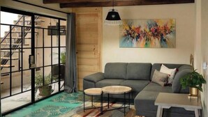 Ein Wohnzimmer mit einer grauen Couch, zwei runden Tischen, einem Gemälde und einer sichtbaren Treppe durch eine Schiebetür.