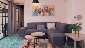 Ein modernes Wohnzimmer mit einem grauen Ecksofa, zwei runden Couchtischen und einem farbenfrohen, abstrakten Gemälde an der Wand.