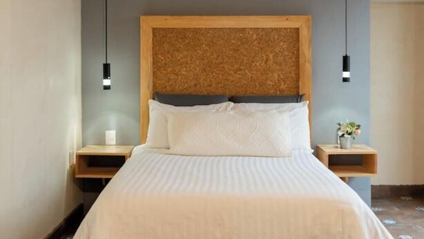 Een net opgemaakt bed met een houten hoofdbord, twee nachtkastjes, en een kleine plant op één van de nachtkastjes.