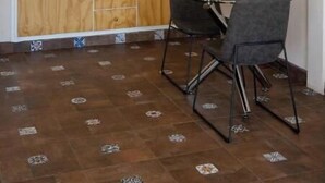 Een kleine keuken met patroontegels, houten kastjes en een eethoek met twee stoelen.