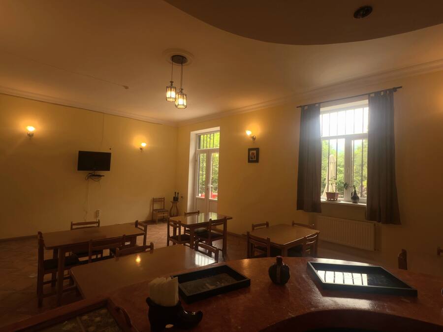 A dining area with wooden furniture, a flat-screen TV mounted on the wall, and a window with curtains.
