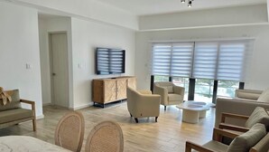 Een moderne woonkamer met een zithoek, een eethoek met een marmeren tafel en een aan de muur bevestigde televisie.