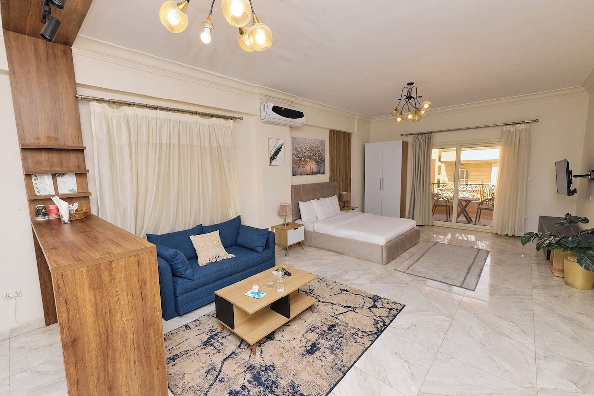 A modern living room with a blue sofa, a wooden coffee table, and a large bed.