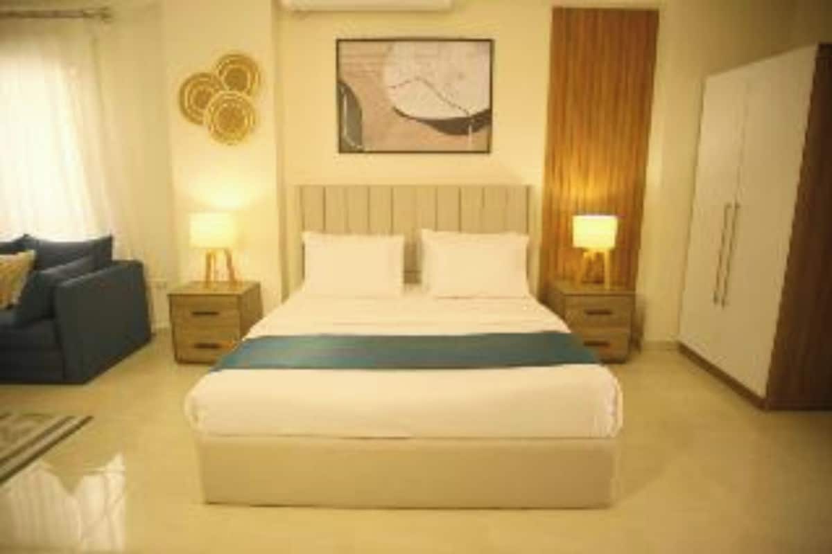 A hotel room with a bed, two bedside tables, a nightstand, a wardrobe, and a wall-mounted artwork.