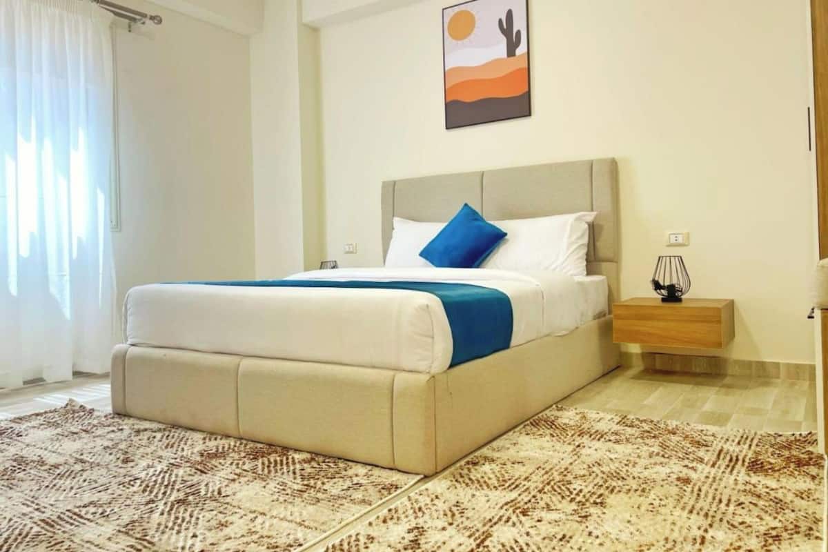 A bedroom with a bed, a nightstand, a lamp, and a painting on the wall.