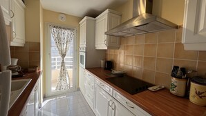 A kitchen with white cabinets, a stainless steel range hood, and a window with curtains.