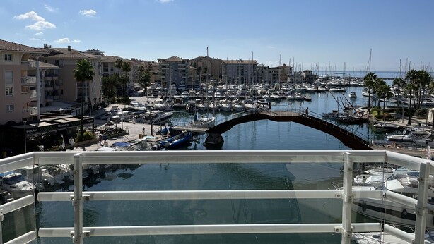 A marina with boats docked, a bridge, and buildings in the background.