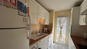 A compact kitchen with a washing machine, a sink, and a window with curtains.