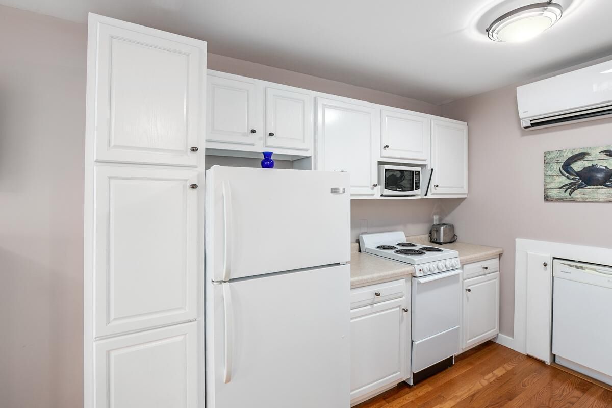 Une cuisine compacte avec des meubles blancs, un four à micro-ondes, une cuisinière et un lave-vaisselle.