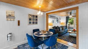 A dining area with a round table and blue chairs, a chandelier, and a fire extinguisher on the wall. - "cozy Cottages" Blue Cottage-hot Tub/town! (Saugatuck)