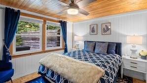 A bedroom with a wooden ceiling, a bed with patterned bedding, two bedside lamps, and a window with curtains. - "cozy Cottages" Blue Cottage-hot Tub/town! (Saugatuck)