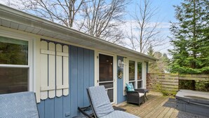 A covered deck with a chair and table, a small round table, and a covered patio area with a bench. - "cozy Cottages" Blue Cottage-hot Tub/town! (Saugatuck)